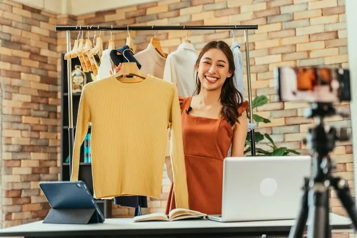 Woman live-streaming while selling clothes online, illustrating how to make extra money during tough economic times through side hustles.