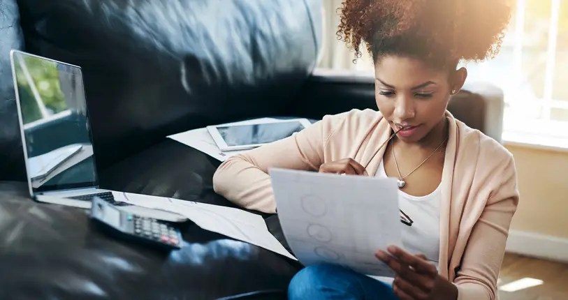 Young woman reviewing financial documents at home with a laptop and calculator, planning how to manage student loans and budget effectively.