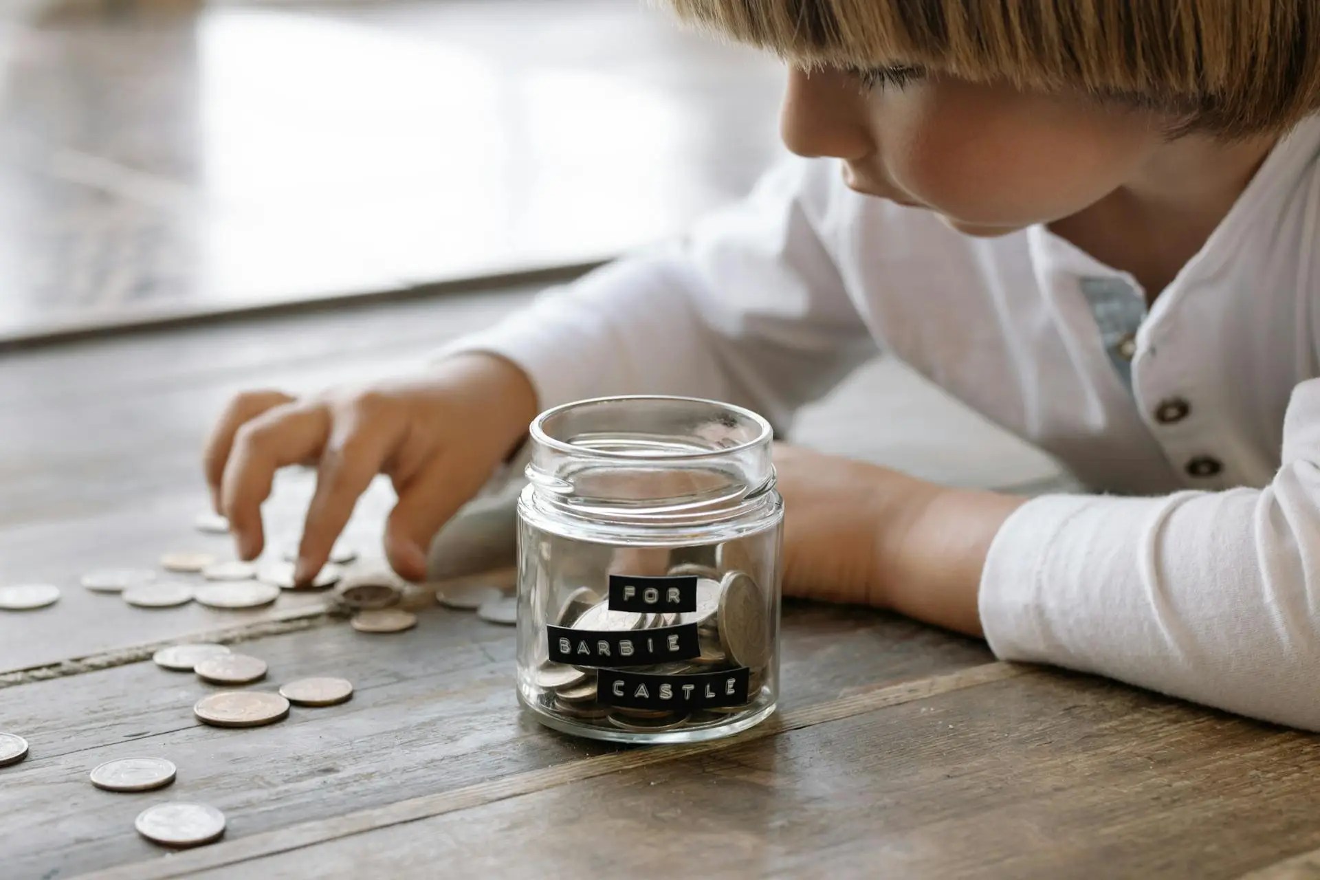 Young child learning to teach financial literacy to the next generation by counting coins and saving in a labeled jar.