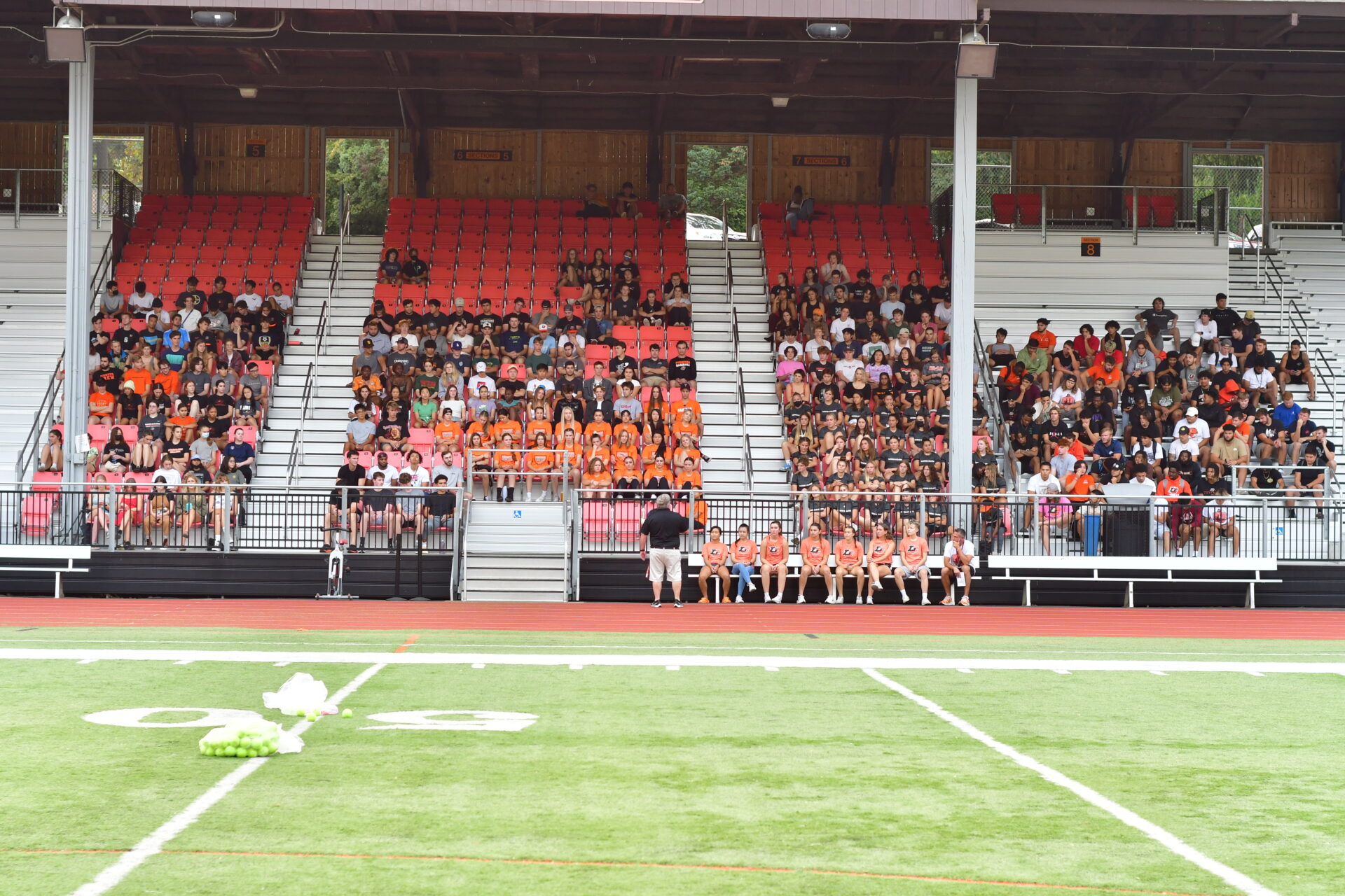 Students and coaches sitting in the bleachers across the football field.