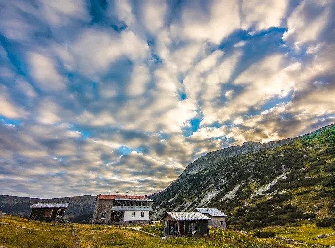 Streaked clouds over a mountain valley with small huts on the grassy slope below