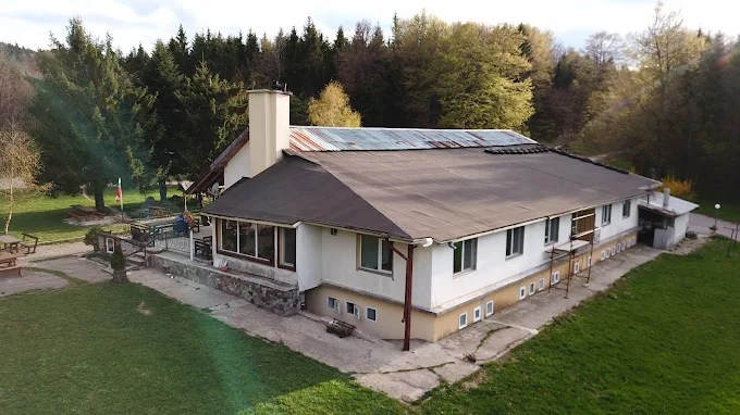 Partizanska Pesen hut, a single-storey white building with roof solar panels at the forest edge