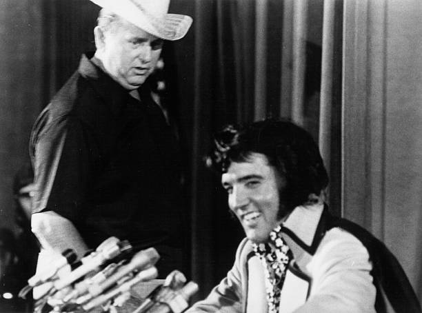 Rock and roll singer Elvis Presley holds court at a press conference to publicize his show at Madison Square Garden later that night while Colonel Tom Parker looks on at the Hilton Hotel on June 9, 1972 in New York City, NY. (Photo by Michael Ochs Archives/Getty Images)