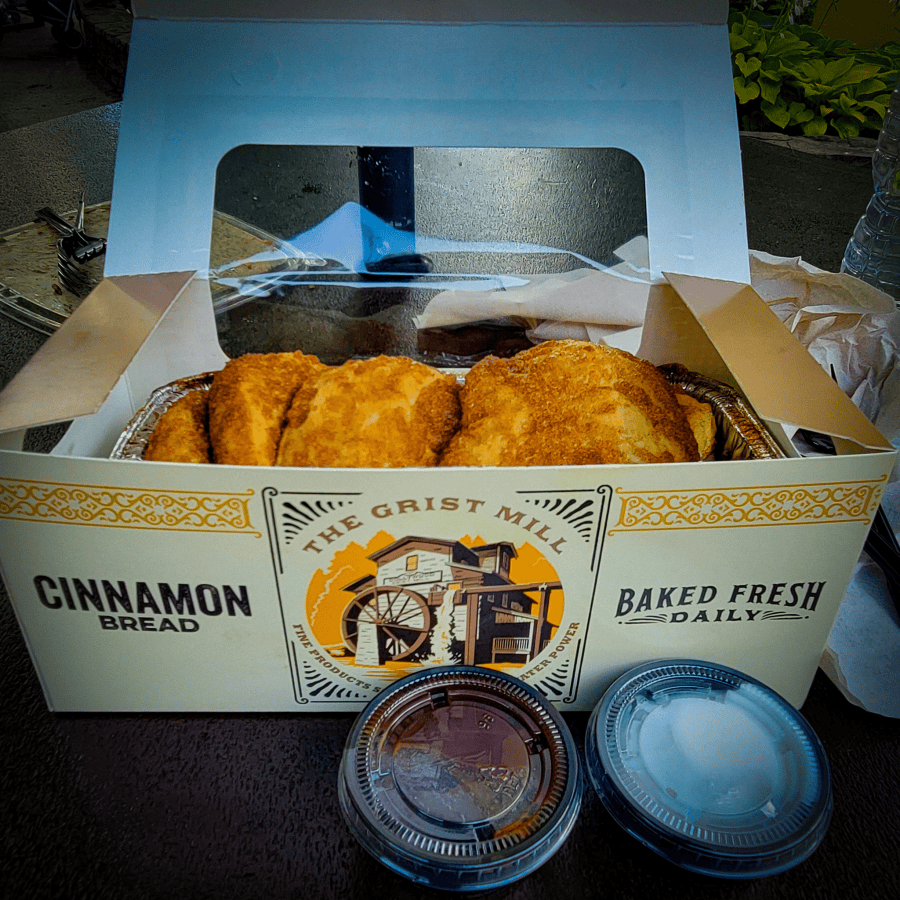 A box filled with fluffy cinnamon bread. Bread box says The Grist Mill. To plastic containers with icing sit in front. Tips for Visiting Dollywood. MPA Project Travels. 