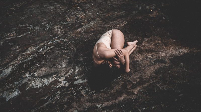 A minimalistic outdoor shot of a woman in a curled position, evoking solitude and introspection.