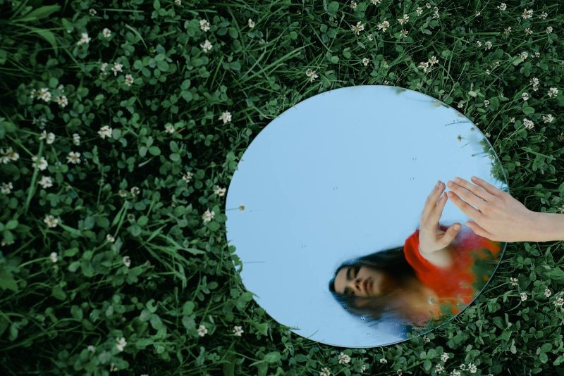 Artistic shot of a woman reflected in a mirror placed on grass