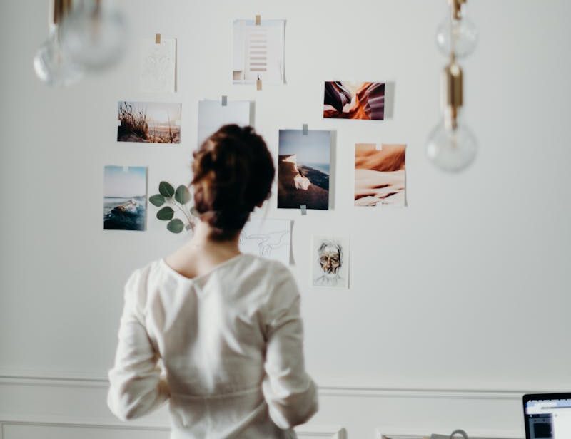 Woman in white top examining mood board under hanging lights in a modern interior design setting.
