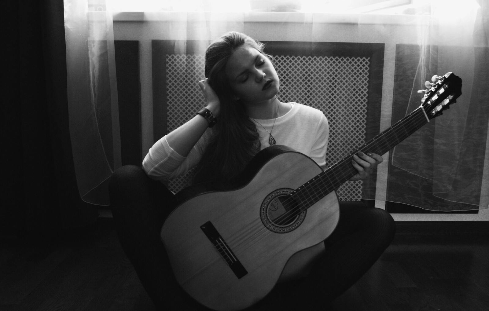Elegant black and white photo of a woman playing classical guitar indoors.
