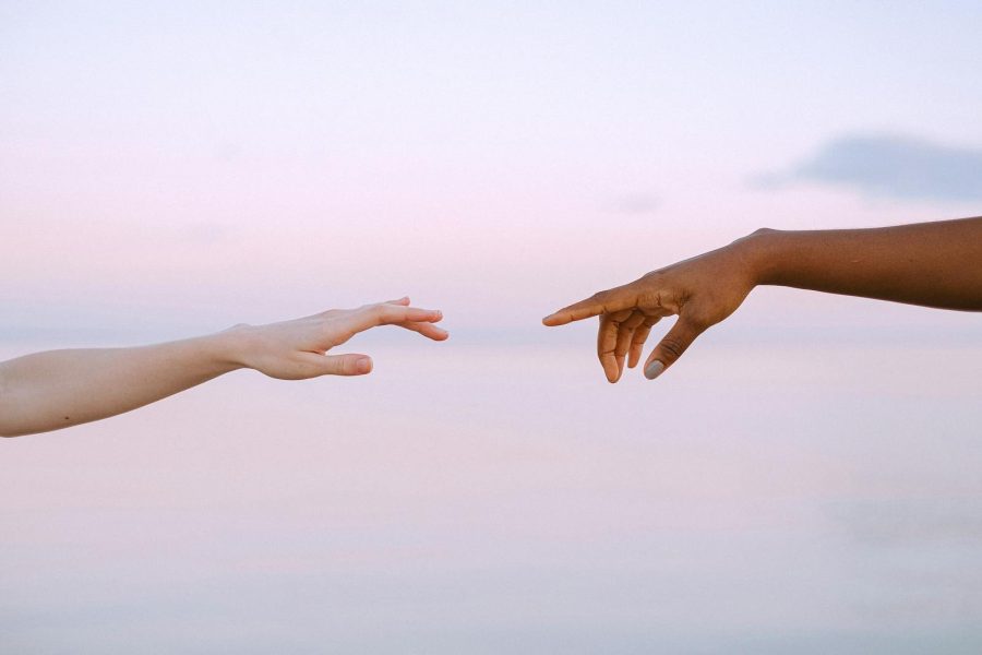 Two diverse hands reaching out across a pastel horizon, symbolizing unity and connection, or separation