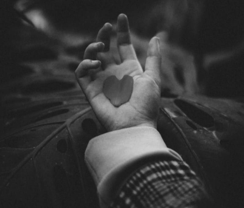 A black and white image of a hand holding a heart-shaped object, symbolizing love.