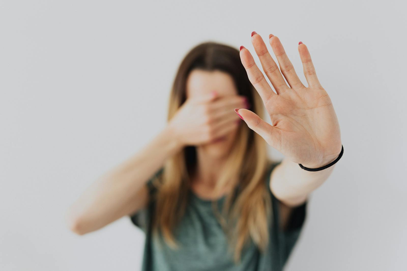 A woman covers her face with her hand in a stop gesture, evoking a sense of fear and protection.