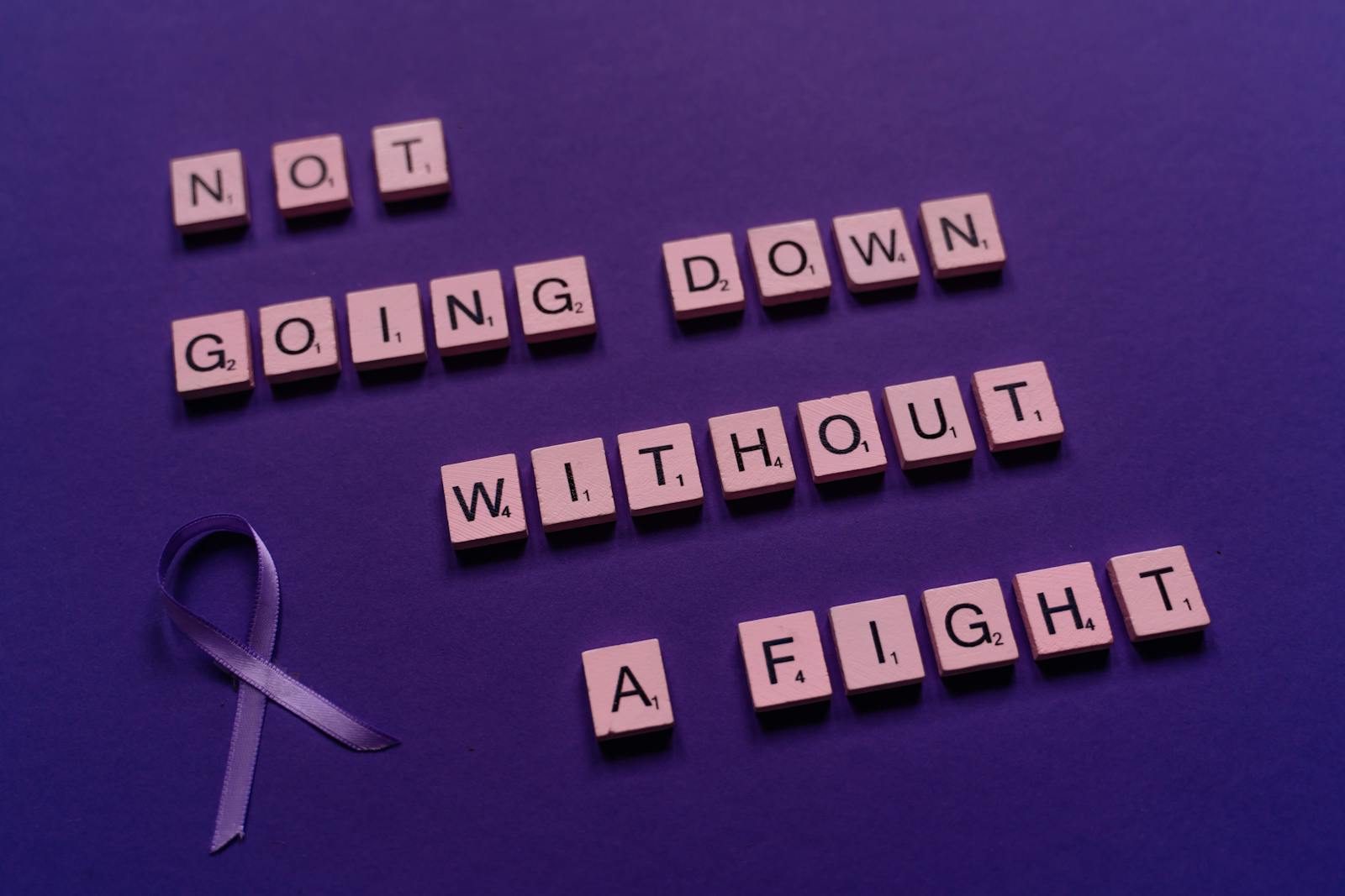 An inspirational quote made from Scrabble tiles alongside a purple awareness ribbon.