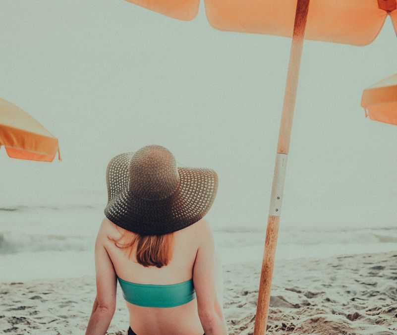 Woman sitting under a beach umbrella, enjoying a sunny day by the sea.
