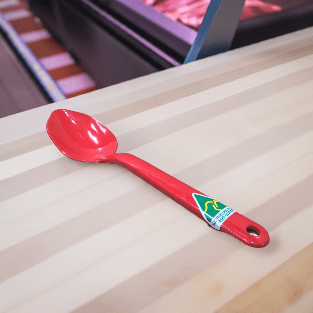 Red food-grade plastic spoon on a wooden countertop, showcasing MTA Products' durable kitchenware designed for professional and home use.