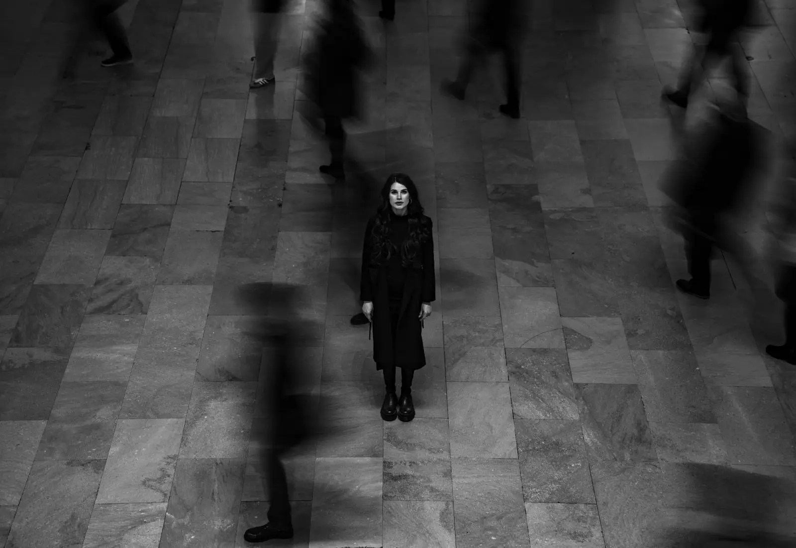 A woman standing still in a busy railway station while commuters blur past her