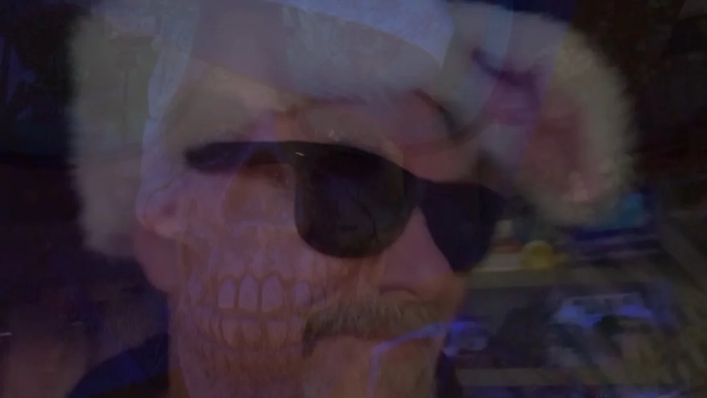 A person wearing sunglasses and a fuzzy hat, with a ghostly skull overlay and a blurred background.