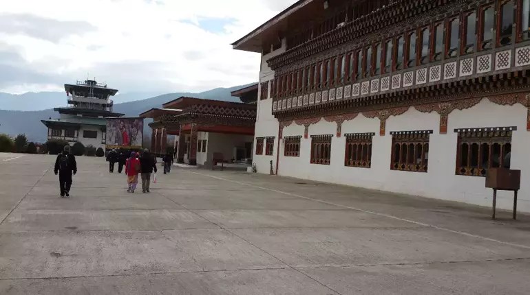 Bhutan'daki bir havaalanında yürüyen insanlar ve geleneksel mimari binalar