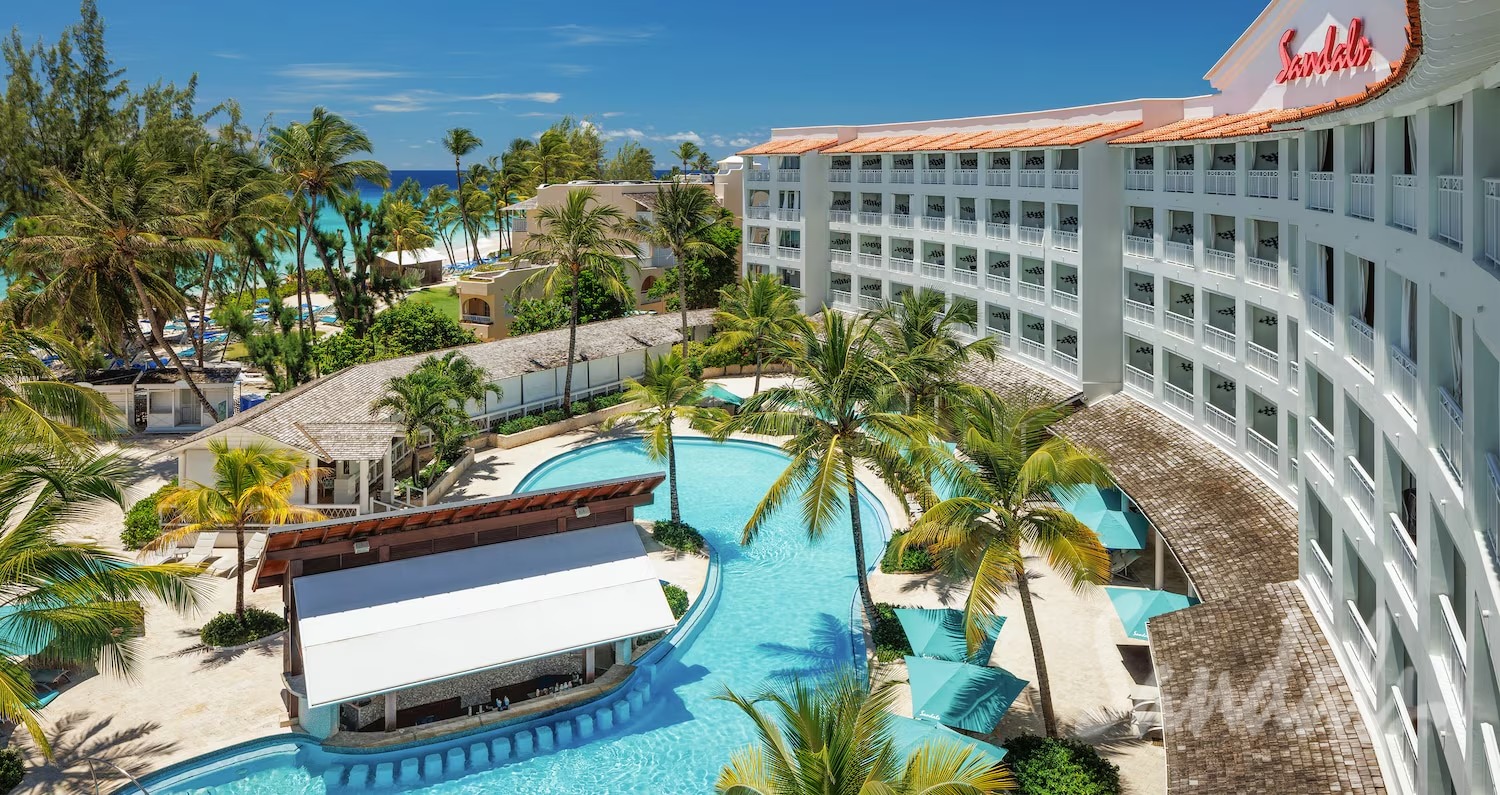 A tropical resort with a curved white hotel building, palm trees, and a turquoise pool near the ocean.