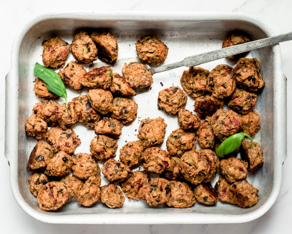 overhead shot of a baking dish with small vegetarian meatballs, and basil leaves