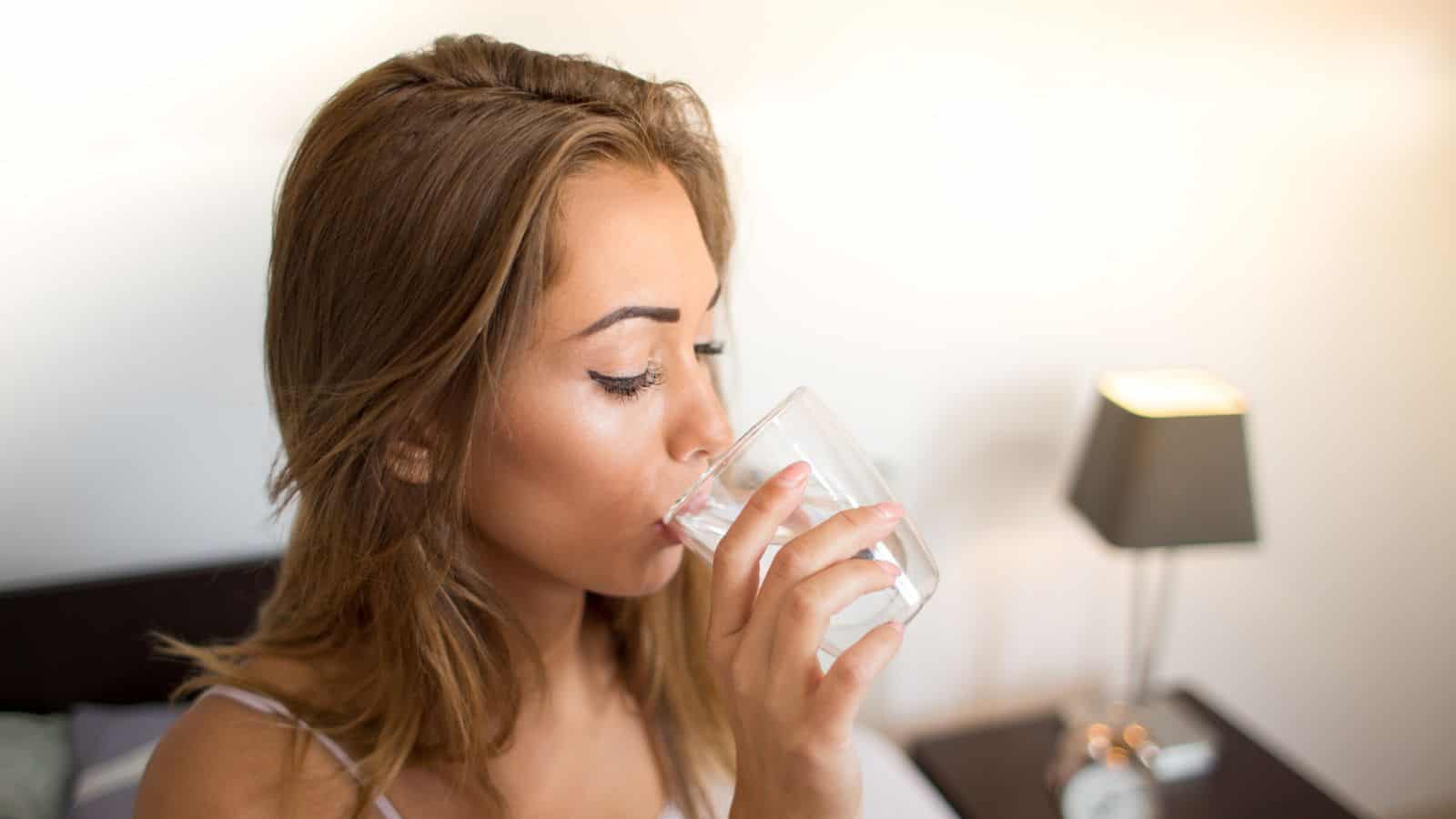 Woman drinking a glass of water while sitting on her bed