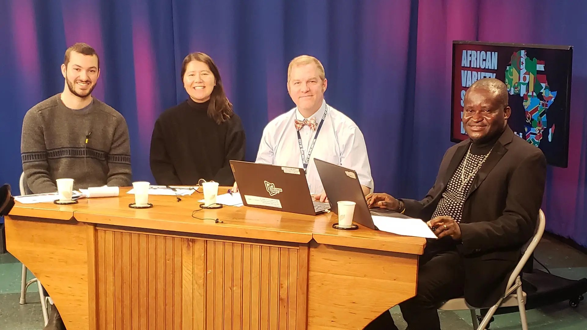 four people behind a desk on a TV set