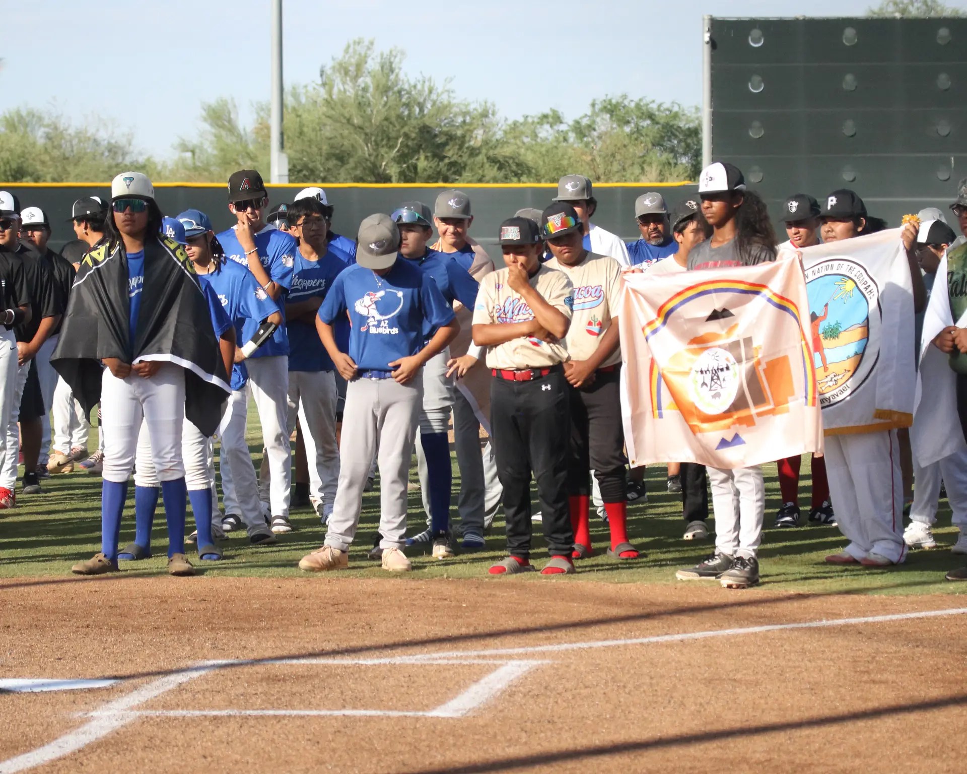 Native American youth baseball players stand united on the field, holding tribal flags at the Na7ive Na7ions National Tournament.