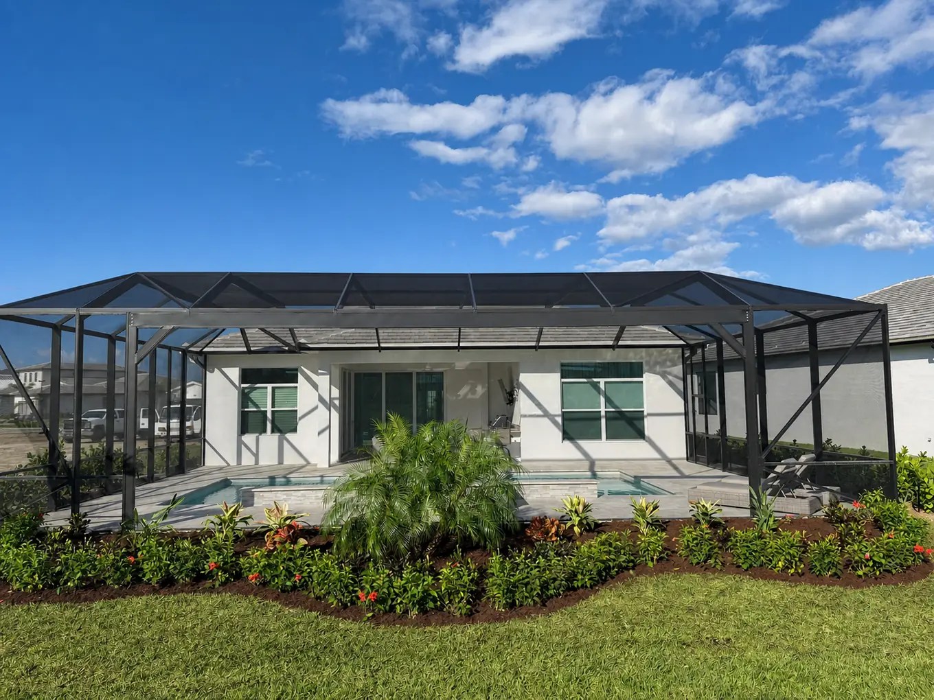 Wide view of an Astor Creek backyard with layered tropical planting, palms, mulch beds, and screened outdoor areas