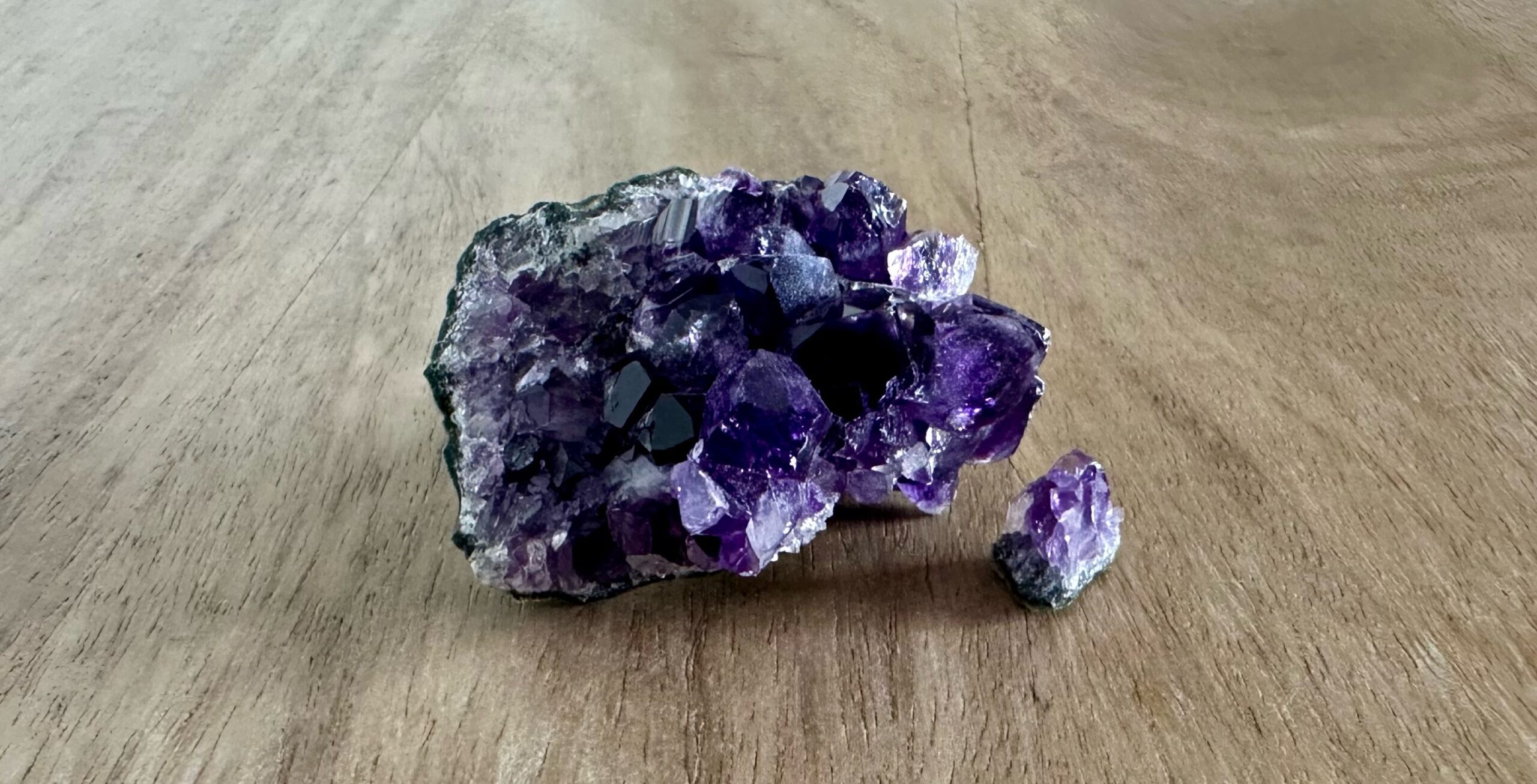 A dark purple amethyst cluster sitting on a wooden table