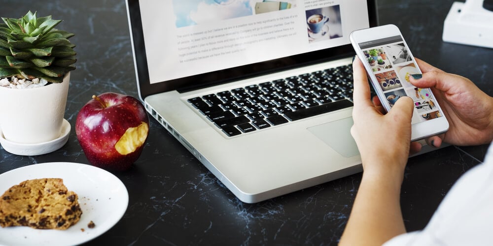 laptop em mesa junto de maçã, prato com biscoito, vaso