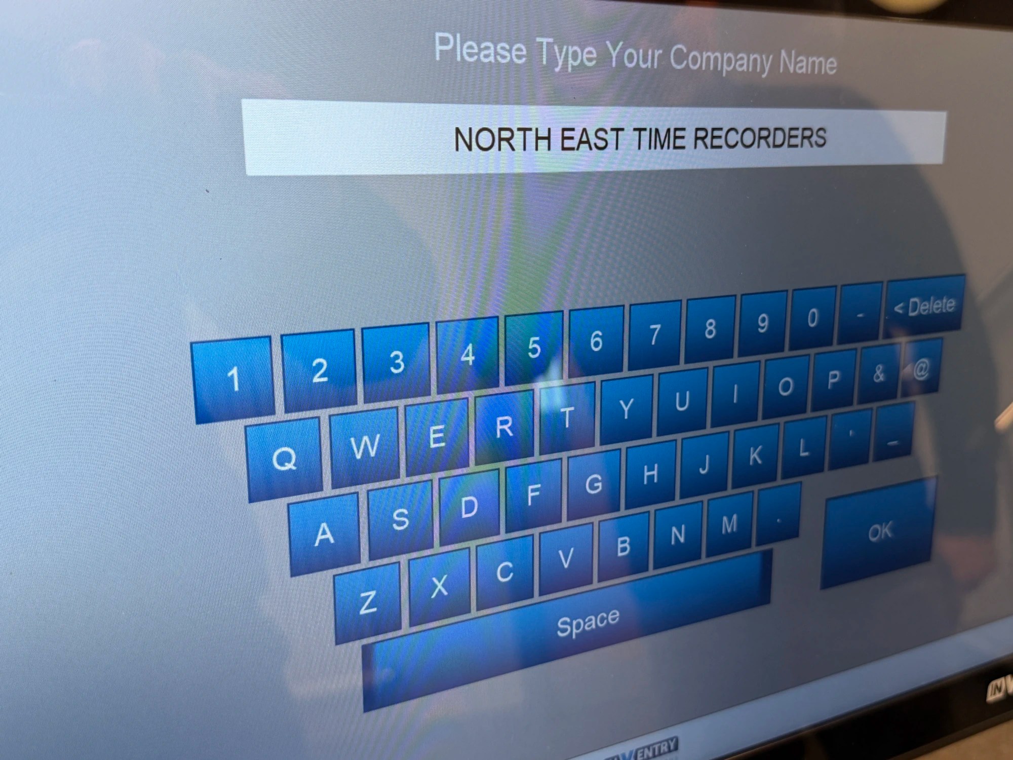 A blue virtual keyboard with a white box above it that says &lsquo;North East Time Recorders&rsquo;.