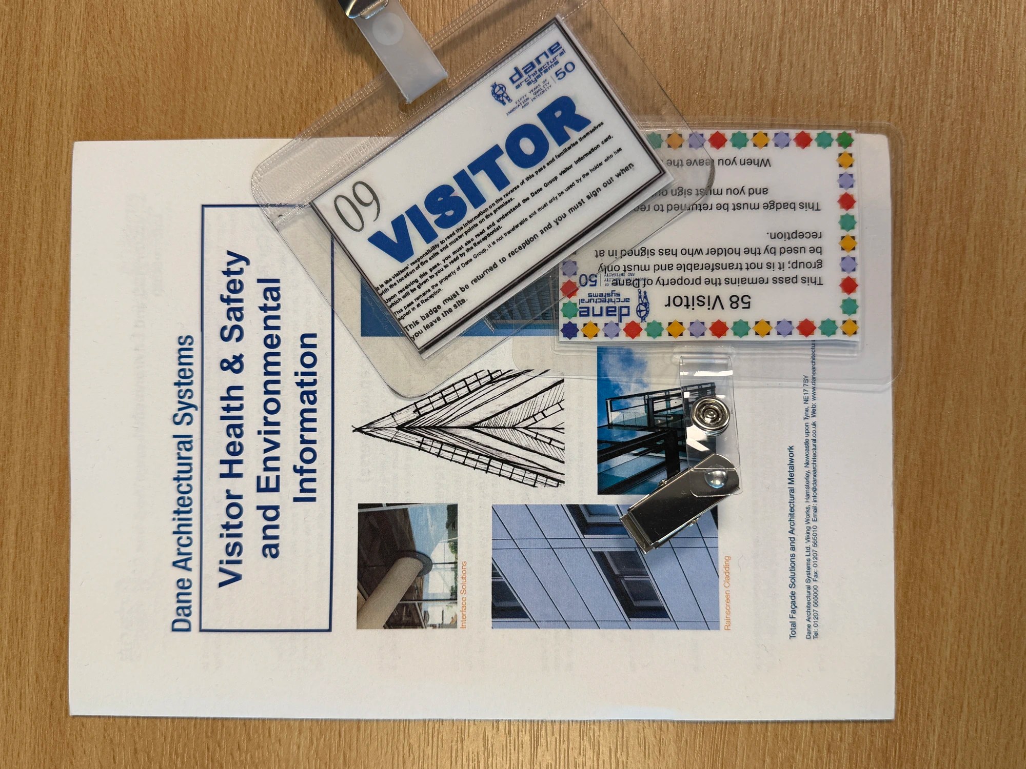 A Dane Architectural Systems visitor pack with a pamphlet and badges.