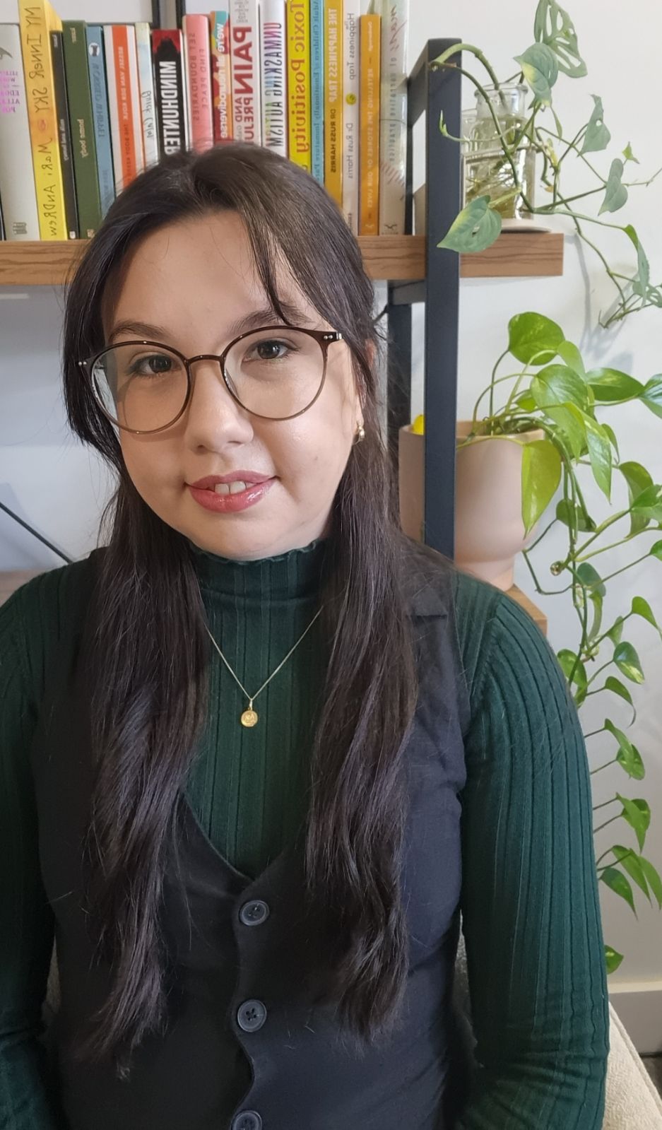 Image of a woman with long brown hair and glasses, wearing a long sleeved green shirt with overalls