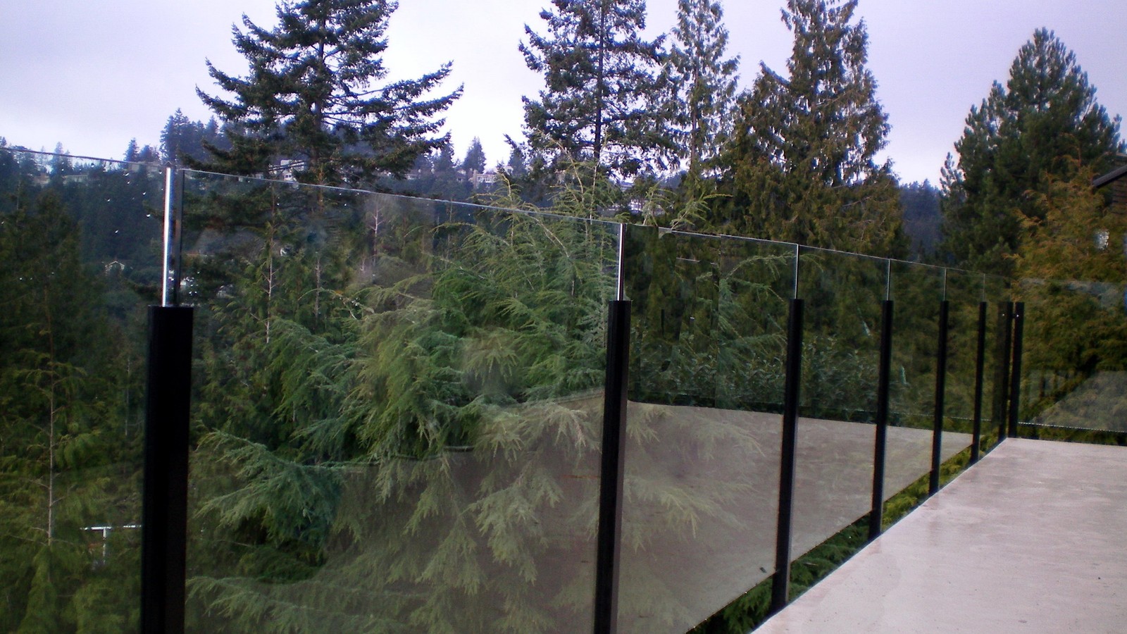 Custom frameless glass deck railing with black steel posts installed at a residential home in West Vancouver