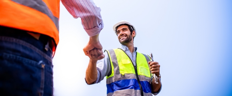 two engineers wearing neon vests greet each other with a fist bump