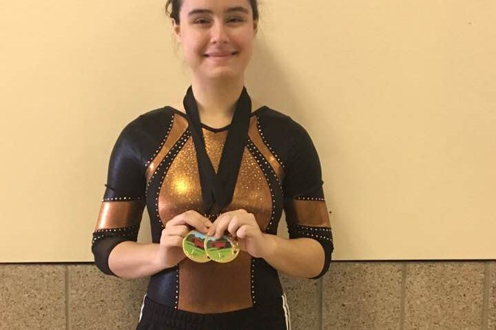 person in leotard holding two first place medals