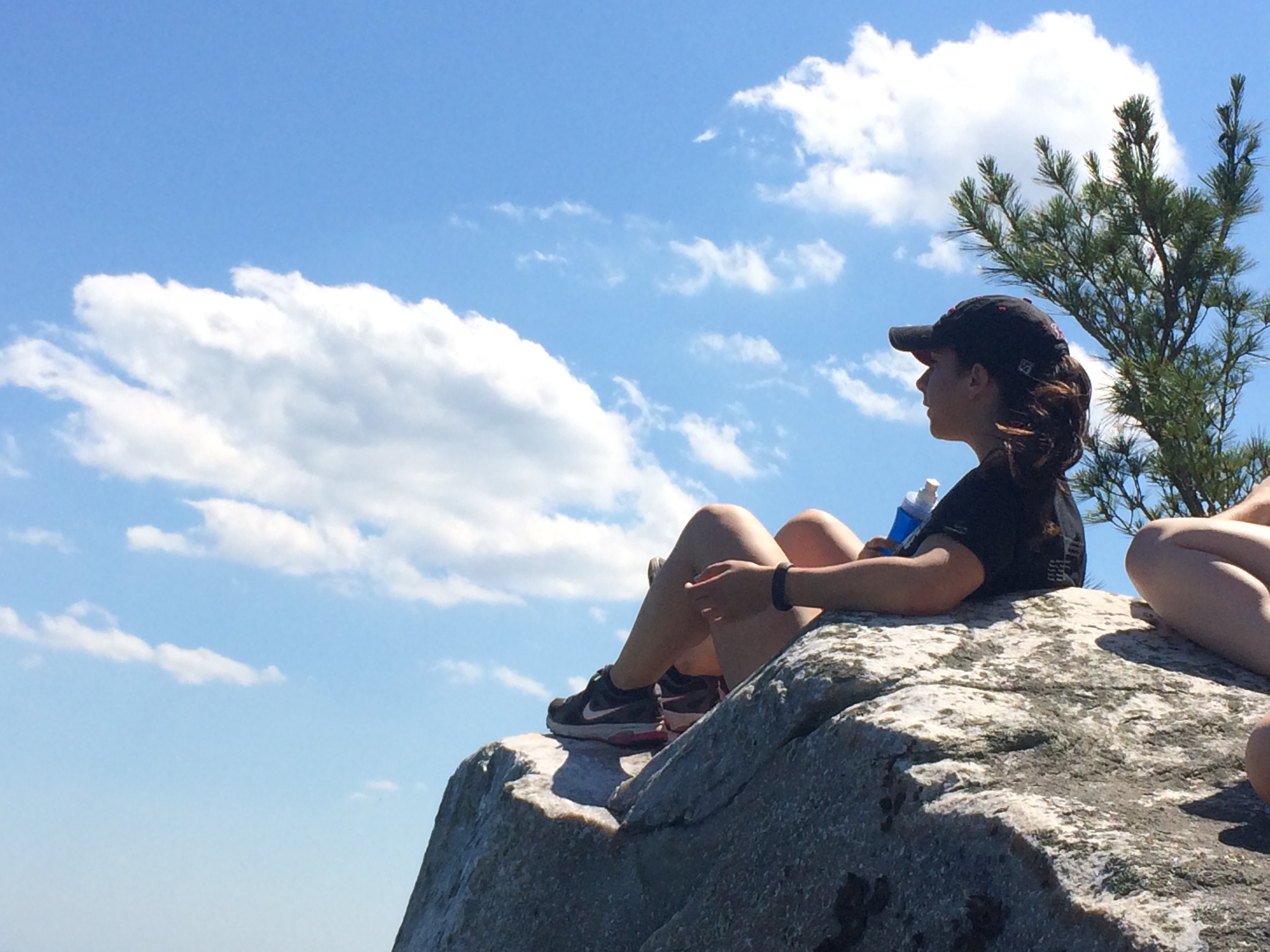 Photo of a woman sitting on a rocky outcrop with a bright blue sky in the background