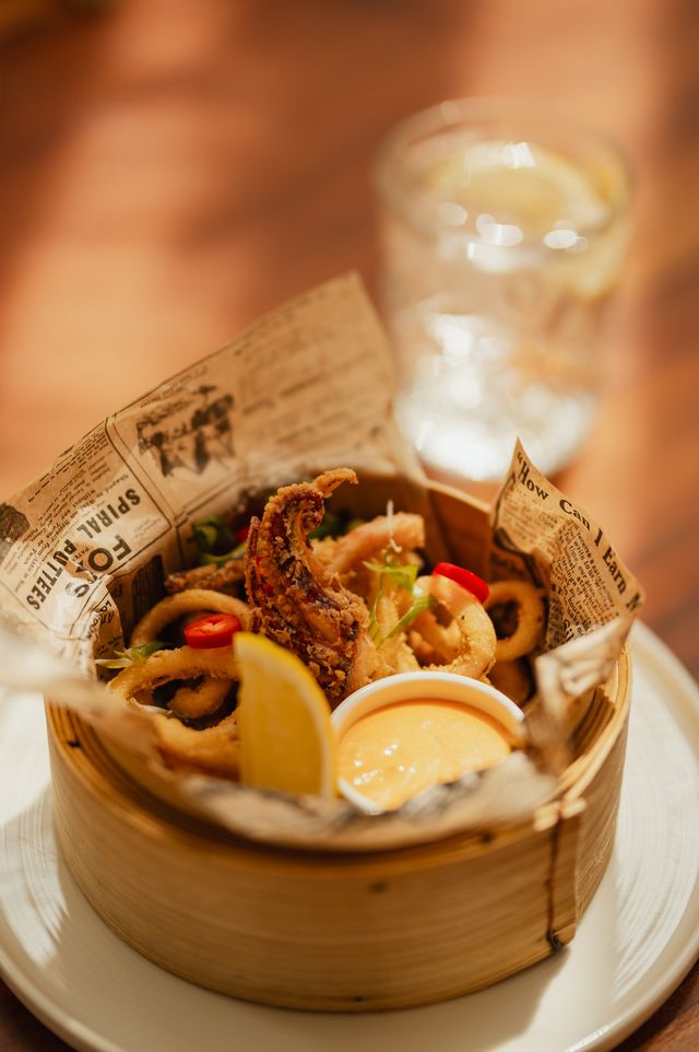Assiette de calamars frits garnis de piments rouges, servis avec une portion de sauce et une tranche de citron.