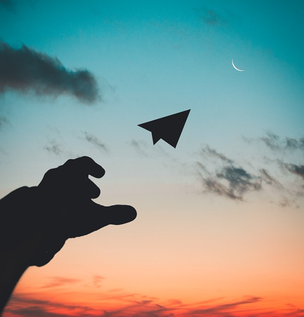 This image shows a shadow of a hand that appears to have sent a paper plane into the sky. It appears to be a beautiful blueish-brown night sky.