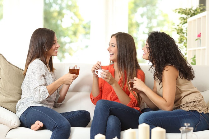 50564338 - three happy friends talking and drinking coffee and tea sitting on a couch at home