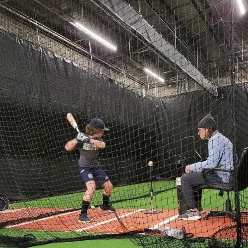 boy swinging a bat at a ball on a tee inside batting cage