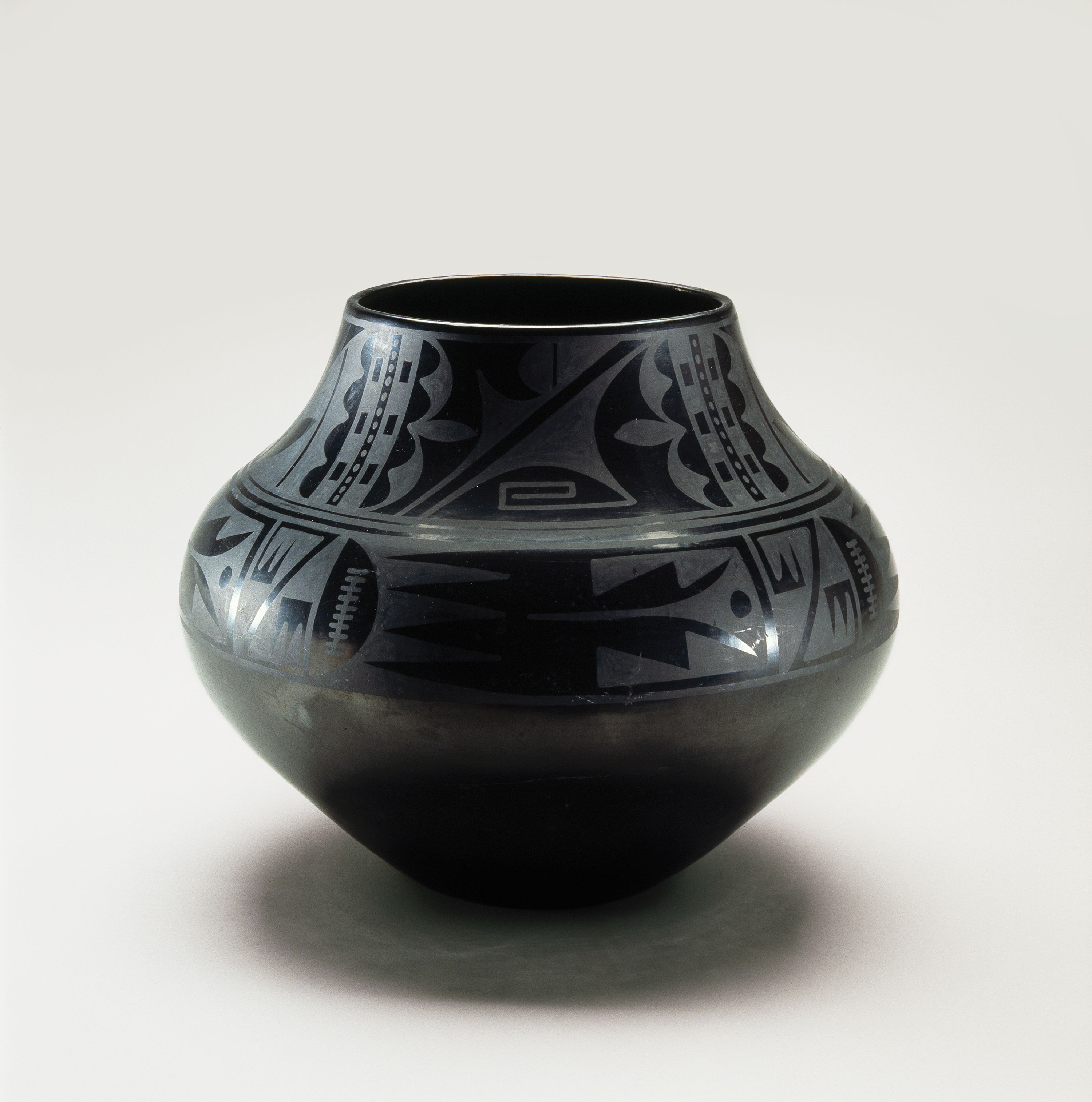 Blackware pottery vessel with a wide mouth and bulbous body that tapers to a narrow base. The pot is adorned with geometric tribal patterns presented in a matte finish on the glossy surface.
