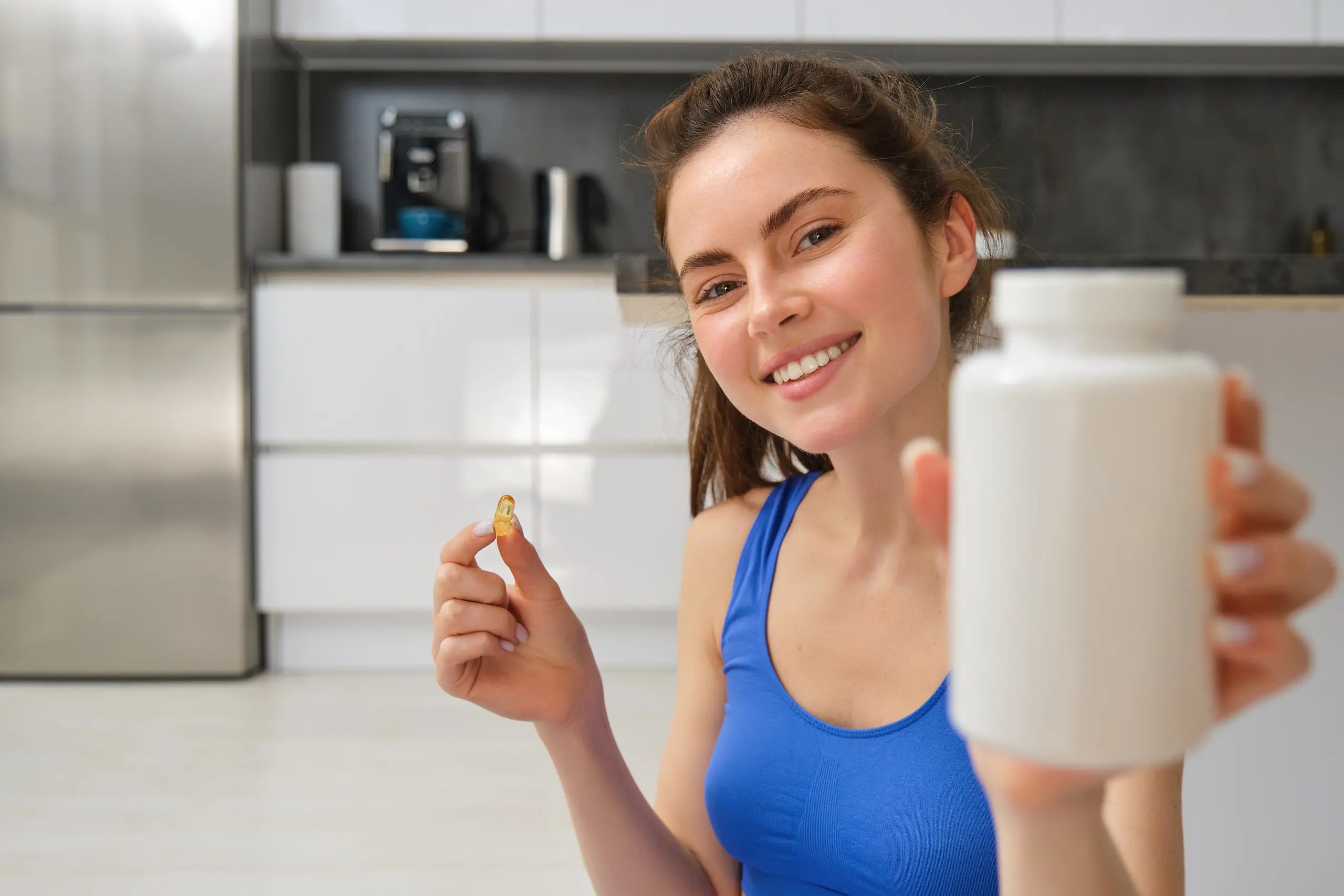 Mujer con top azul sosteniendo un bote blanco de suplementos.