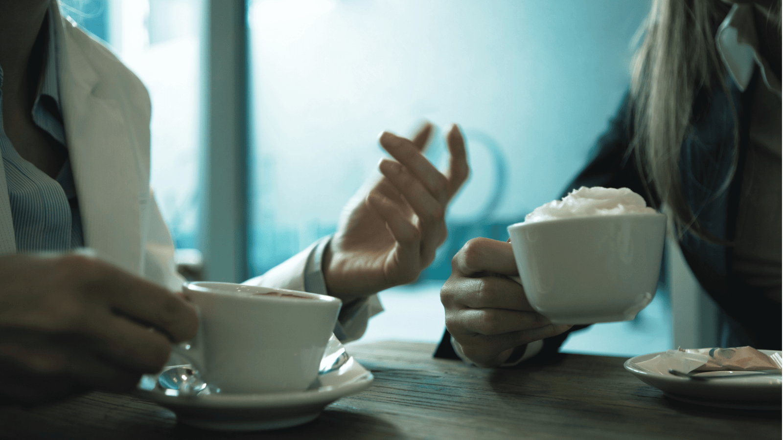 Close up of two people's hands with coffee, one person expressing herself with her hands during a conversation.