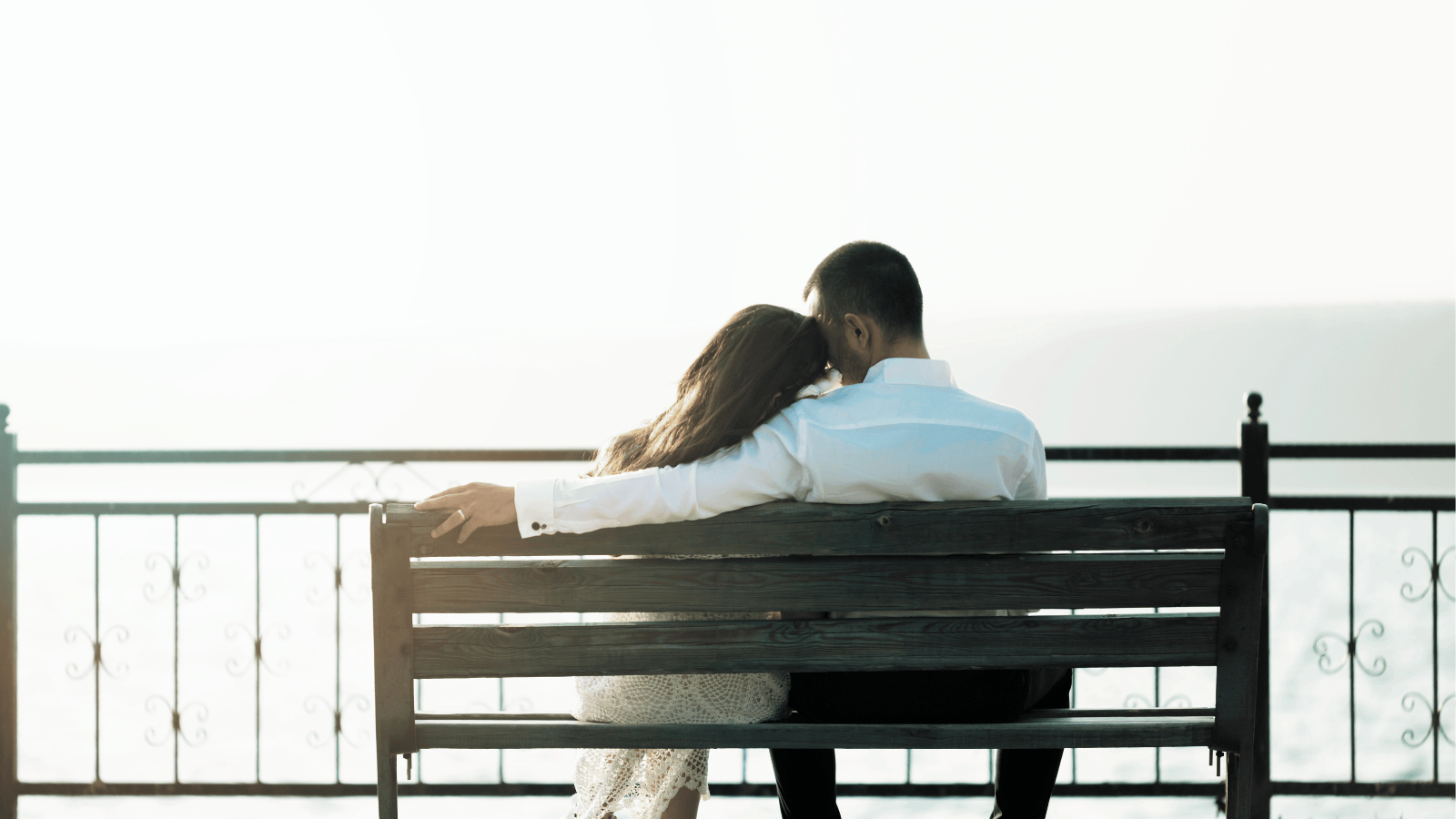 A married couple sitting on a bench, her head on his shoulder, facing away from the camera. Marriage and sobriety can be complicated.