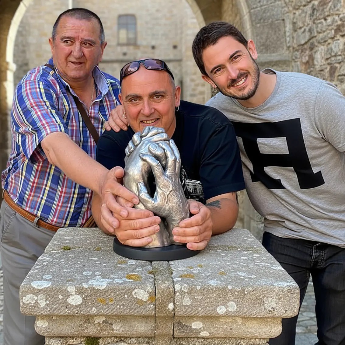 El actor Ahikar Azcona (conocido por su papel en La casa de papel) posa junto a su padre y abuelo, sosteniendo una escultura de manos intergeneracional de No Me Sueltes Nunca. La pieza de lifecasting captura el lazo familiar de tres generaciones. Ideal para promocionar regalos originales y el valor de los recuerdos de familia."