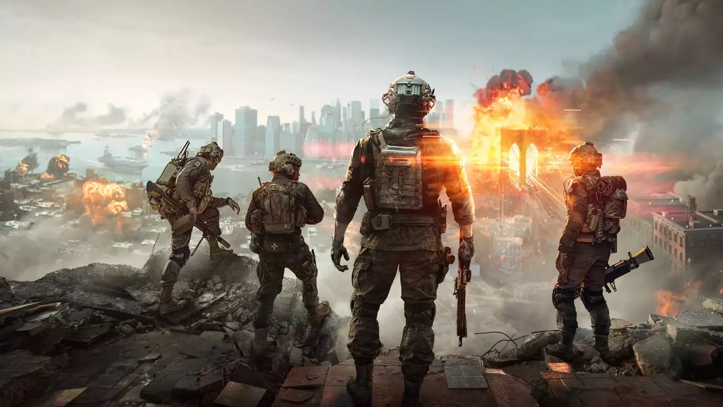 Promotional key art for Battlefield 2042: Four heavily armed specialists in tactical gear stand on a rocky outcrop overlooking a devastated urban battlefield, with massive explosions, burning buildings, collapsing structures, and thick smoke rising against a hazy sky.