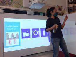 Une photo d'une présentatrice devant le tableau avec la présentation sur la pollution plastique et la réduction des déchets.