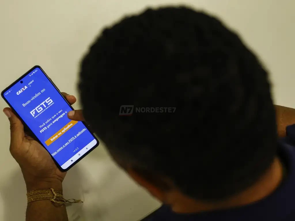 Pessoa segurando um celular com a tela do aplicativo oficial do FGTS aberta exibindo dados de saldo.