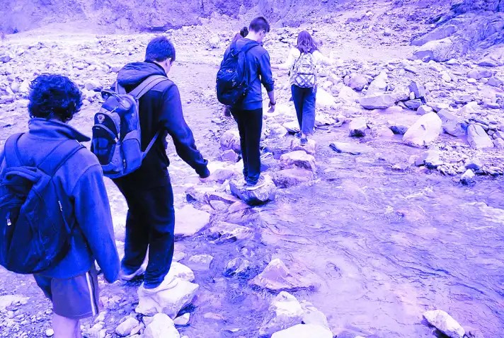 Excursionistas cruzando un río, sobre piedras.