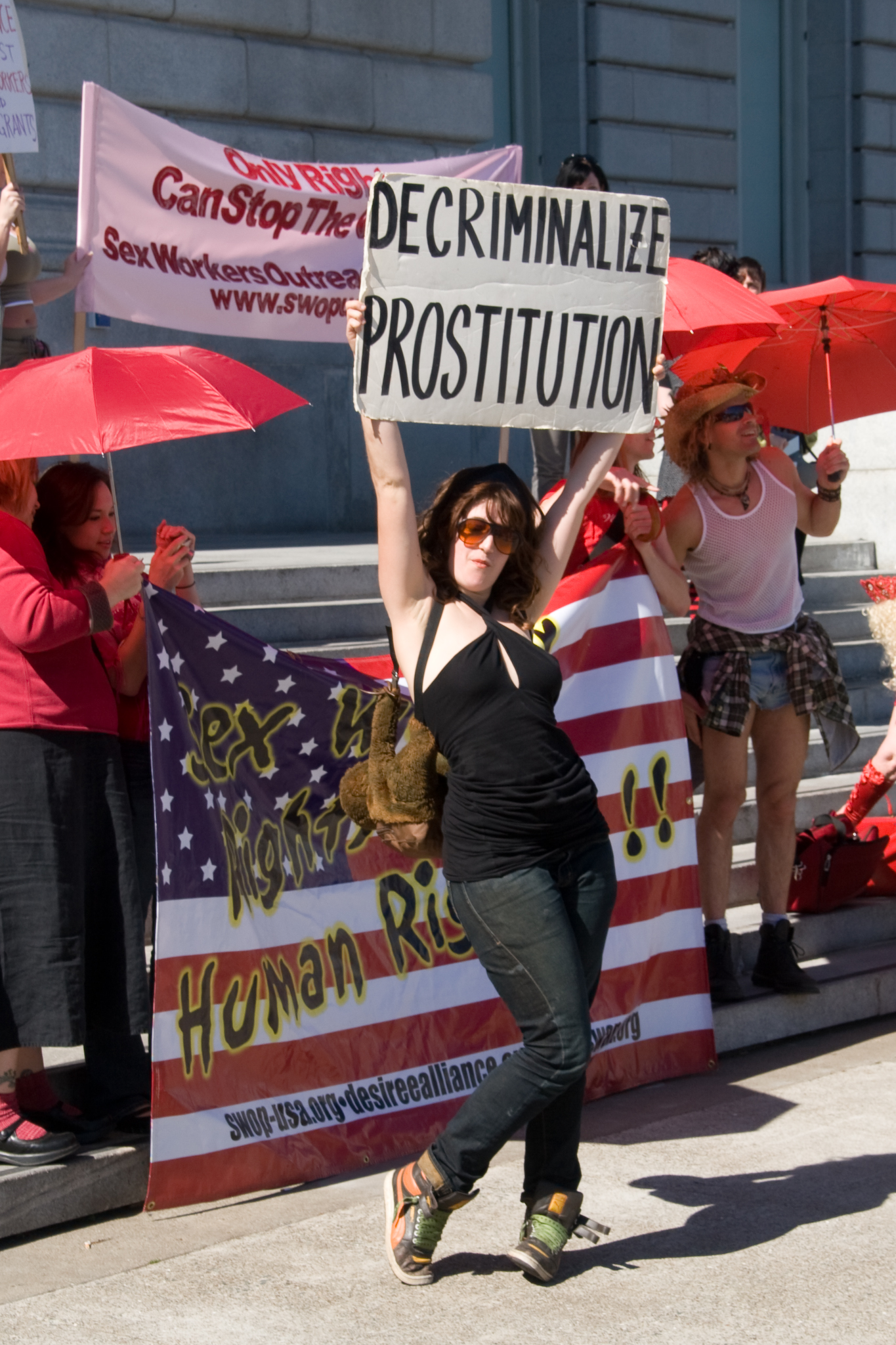 A woman wearing sunglasses standing in front of national flag, holding a slogan